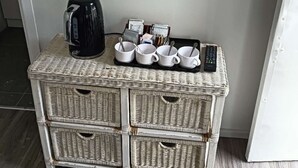 A wicker storage unit with multiple compartments, a black electric kettle, white cups, and a remote control. - 1 Bedroom garden chalet 7B  (Rotorua)