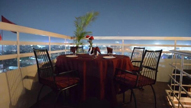 A balcony with a table set for two, chairs, and a vase with flowers. - Hotel Somdeep Palace (Indore)