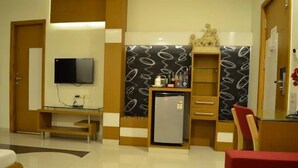 A compact hotel room with a flat-screen TV, a refrigerator, a small table, and a chair. - Hotel Somdeep Palace (Indore)