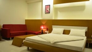 A hotel room with a large bed, a red sofa, a small table, and a wall-mounted lamp. - Hotel Somdeep Palace (Indore)