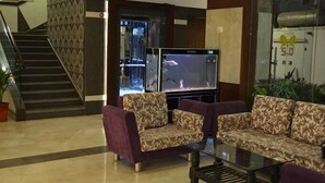 A lobby with patterned sofas, a glass coffee table, and a fish tank. - Hotel Somdeep Palace (Indore)