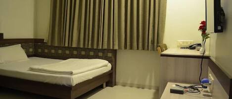 A hotel room with a bed, a desk with a telephone, and a wall-mounted TV.