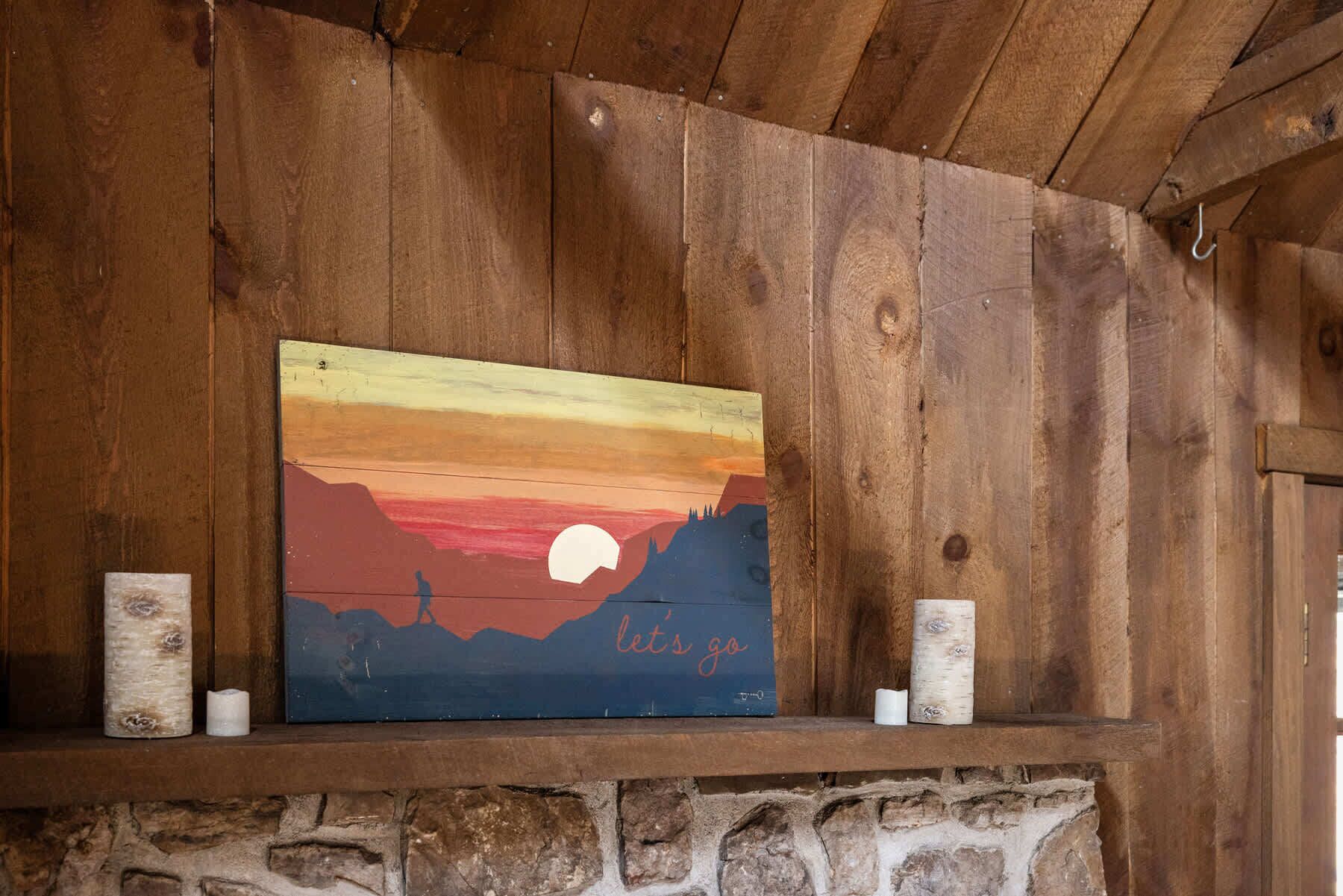 Een rustieke houten wand met een geschilderd zonsondergang tafereel en de tekst 'let's go' op een plank.