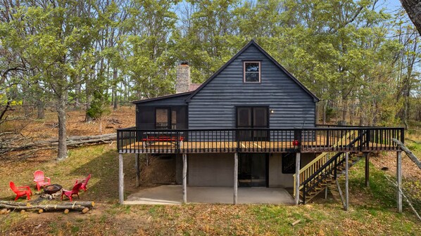 A cabin with a balcony, a fire pit, and red chairs.