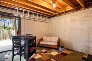 A room with a wooden ceiling, a sofa, a desk with a chair, and a patterned rug.