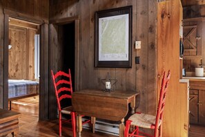 A wooden interior with a dining table, two chairs, a framed map, and a bed.