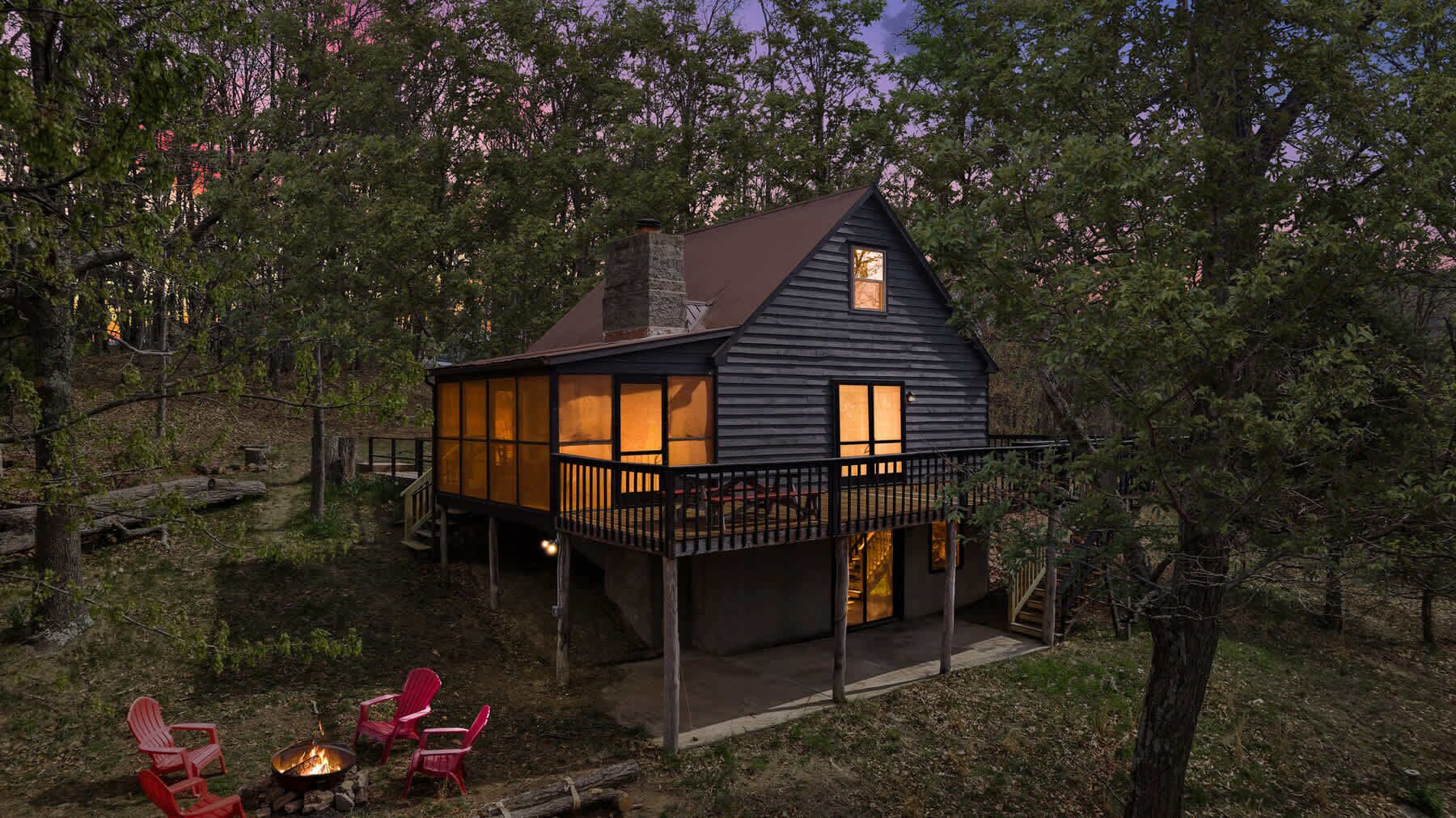 Een chalet met terras, vuurkorf en rode stoelen.