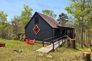 A cabin with a wooden deck, a covered porch, and a large quilt decoration on the wall. - Cozy cabin w/ grill deck & game room (Mathias)