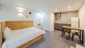 A bedroom with a wooden headboard bed, a small desk with a chair, a kitchenette with a refrigerator, and a door leading to another room. - Gyeongju Nollowa Spa Pension (Gyeongju)