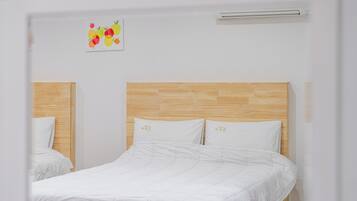 Ett hotellrum med en sänggavel i trä, vita sängkläder och ett konstverk med fruktmotiv på väggen.