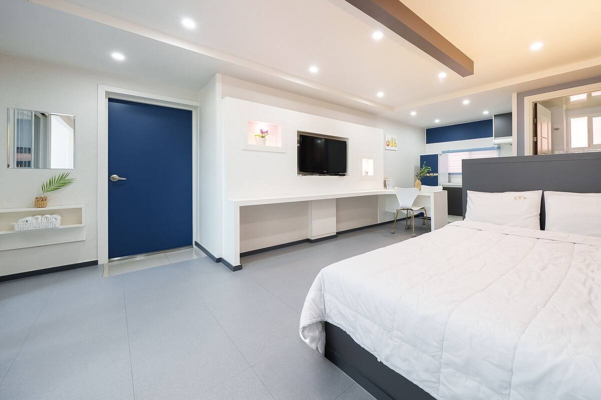 A modern hotel room with a large bed, a TV, a desk, and a bathroom.