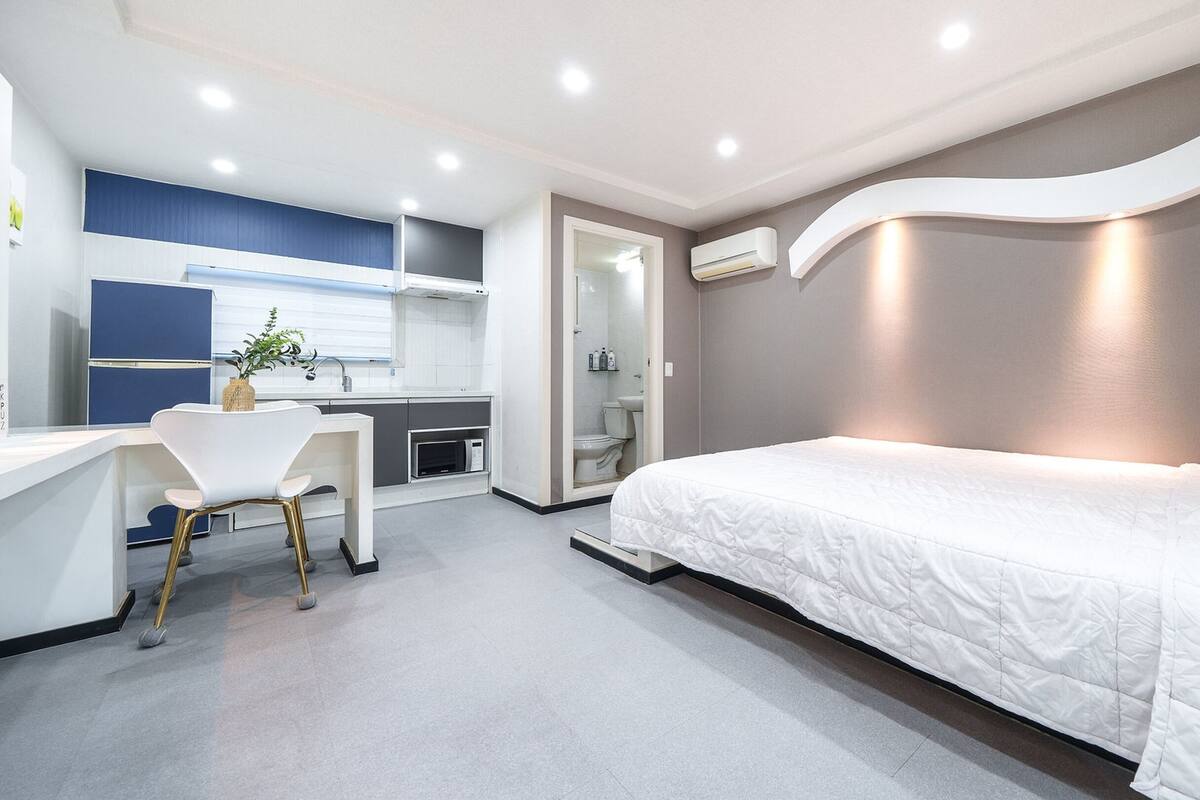 A modern hotel room with a bed, a desk, and a kitchenette.