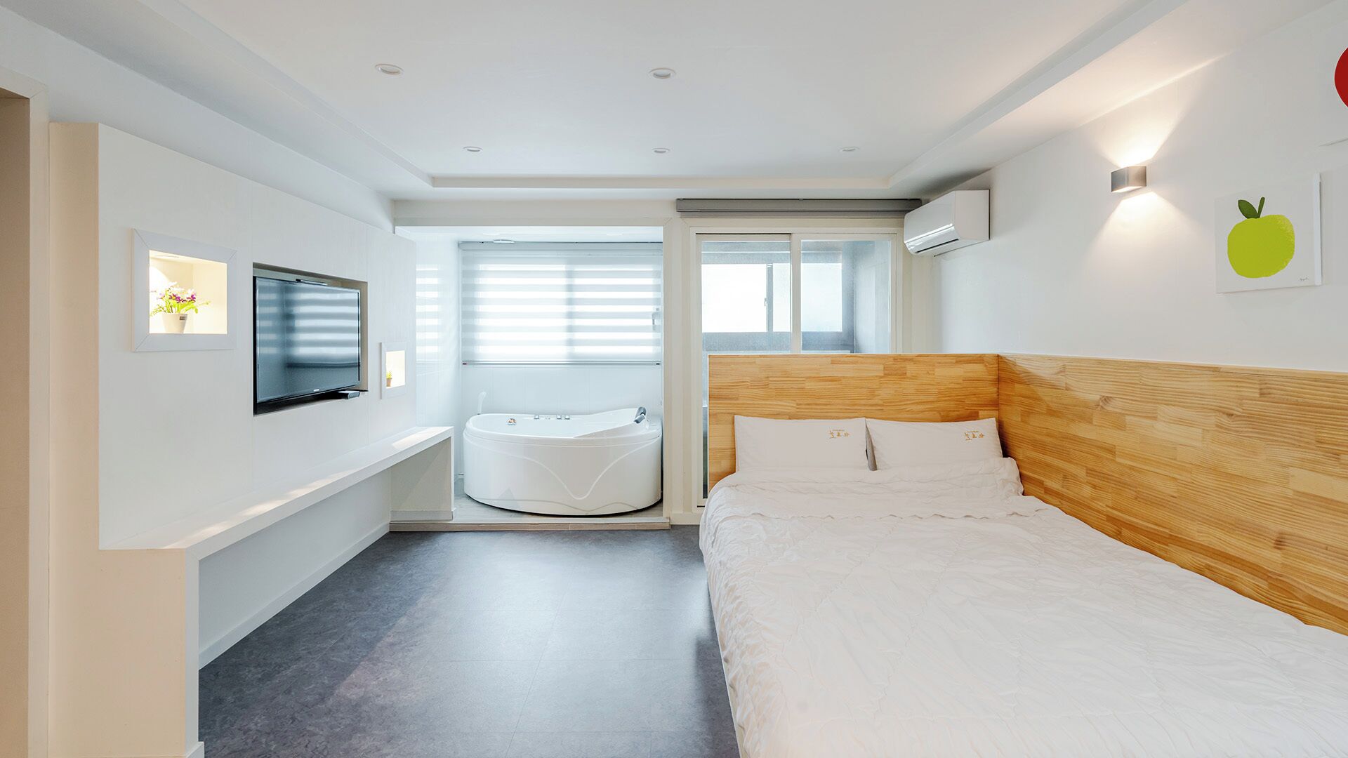 Ein modernes Hotelzimmer mit Bett, Fernseher, Badewanne und einem Fenster mit Jalousien.