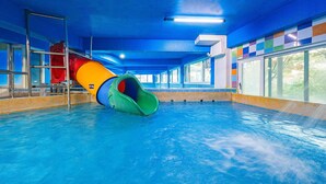 Ein Hallenbad mit bunten Wasserrutschen, klarem, blauem Wasser und Blick ins Freie durch große Fenster.