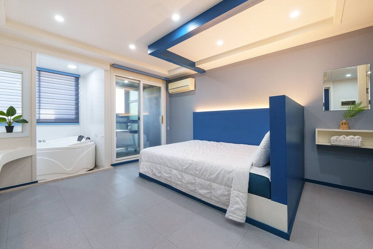 A modern bedroom with a bed, a built-in bathtub, and a sliding glass door leading to a bathroom.
