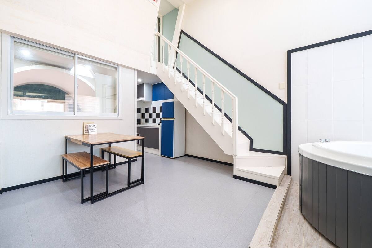 A modern kitchen with a dining area, a staircase, and a bathtub.
