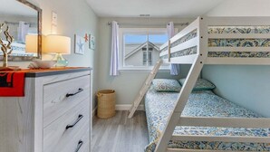 A bedroom with a bunk bed, a dresser with drawers, a mirror, and a window with curtains.