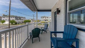 A covered balcony with two Adirondack chairs, a white railing, and a view of neighboring houses.