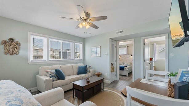 A living room with a sofa, coffee table, and a ceiling fan. There is a dining area with a table and chairs.