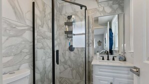 A bathroom with a glass shower enclosure, a white sink with a mirror, and a white vanity with drawers.
