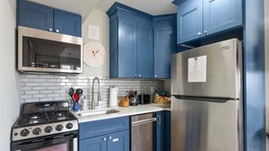 A kitchen with blue cabinets, a stainless steel refrigerator, a stove, and a microwave.