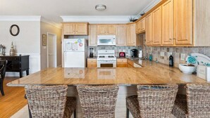 A kitchen with wooden cabinets, a white refrigerator, a microwave, a stove, and a large island with wicker chairs. - Modern 3 Bedroom Condo in a Prime Location (Wildwood)