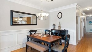 A dining room with a wooden table, chairs, a bench, a chandelier, a mirror, and a clock on the wall. - Modern 3 Bedroom Condo in a Prime Location (Wildwood)