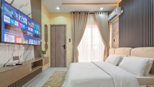 Ein modernes Hotelzimmer mit großem Flachbildfernseher, der eine Auswahl an Filmen zeigt, einem komfortablen Bett mit weißer Bettwäsche, einem Holzschrank und einer Wand mit Marmormuster.