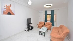 A living room with a flat-screen TV, two armchairs, a sofa, a coffee table, and a painting on the wall.