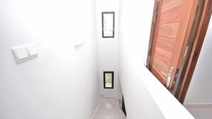 A narrow stairway with white walls, a wooden door at the end, and a small window on the wall.