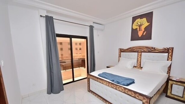 A bedroom with a large bed, a sliding glass door to a balcony, and a painting on the wall.