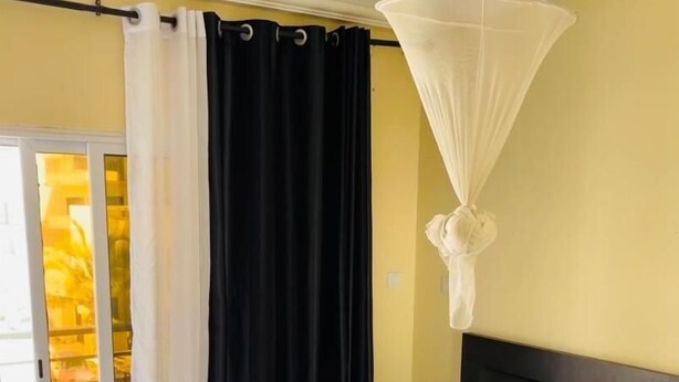 A hotel room with a bed, a nightstand, a white curtain, a black curtain, and a white canopy. - Le Fabuleux- Standing ,SV CITY Virage Yoff, Dakar (Dakar)