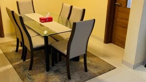 A dining area with a glass table and six chairs, a red tissue box, and a wooden door in the background. - Le Fabuleux- Standing ,SV CITY Virage Yoff, Dakar (Dakar)