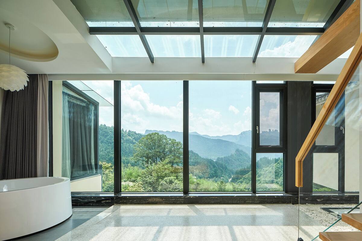 A modern room with a large skylight, a curved white sofa, and a view of a mountainous landscape.