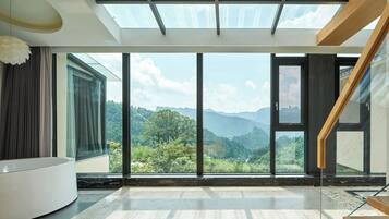 A modern room with a large skylight, a curved white sofa, and a view of a mountainous landscape.