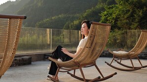 A person sitting on a wicker rocking chair with a view of a lake and hills in the background. - Serenity Valley - Zhangjiajie (Zhangjiajie)