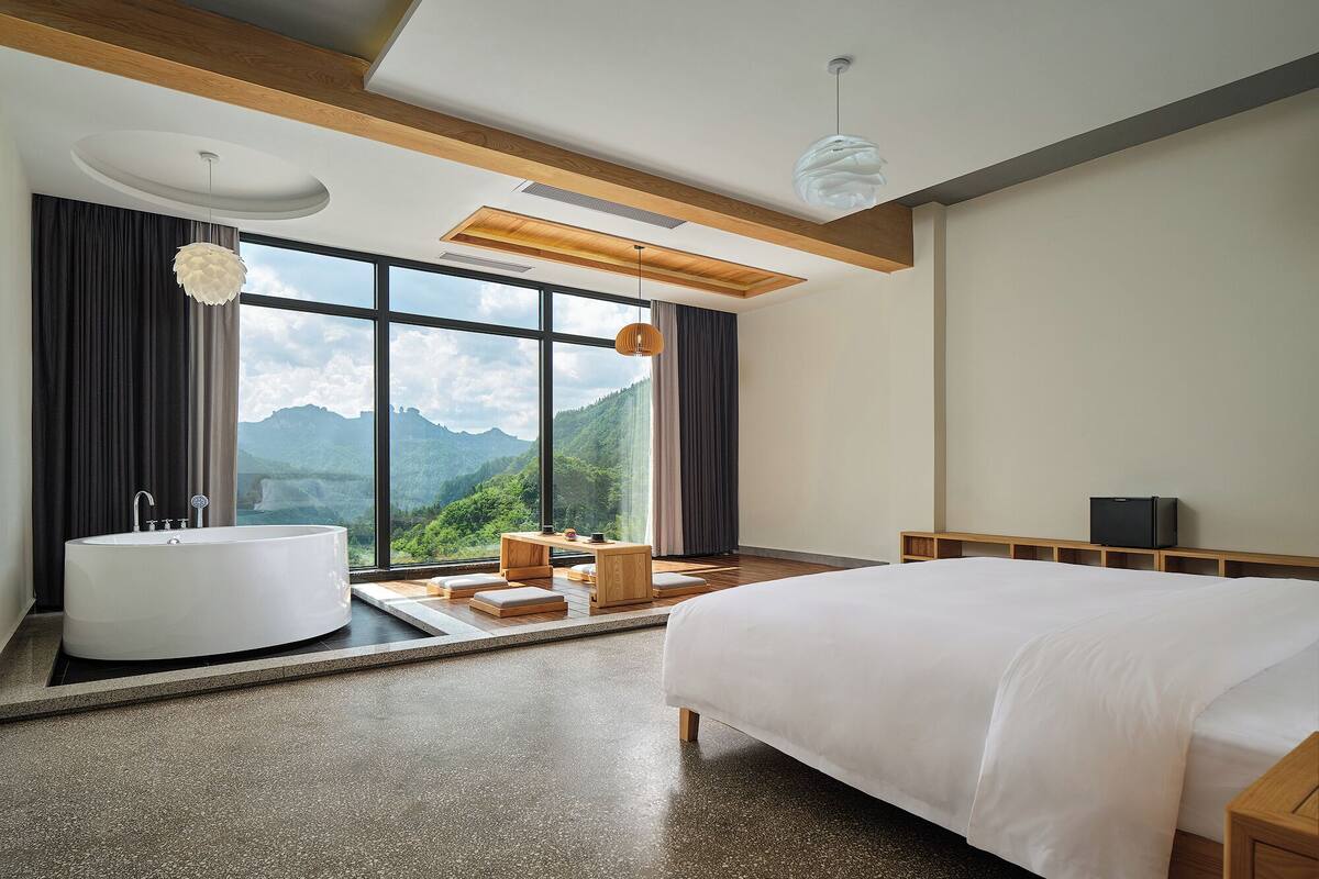 A modern bedroom with a large bed, a bathtub, and a view of mountains.