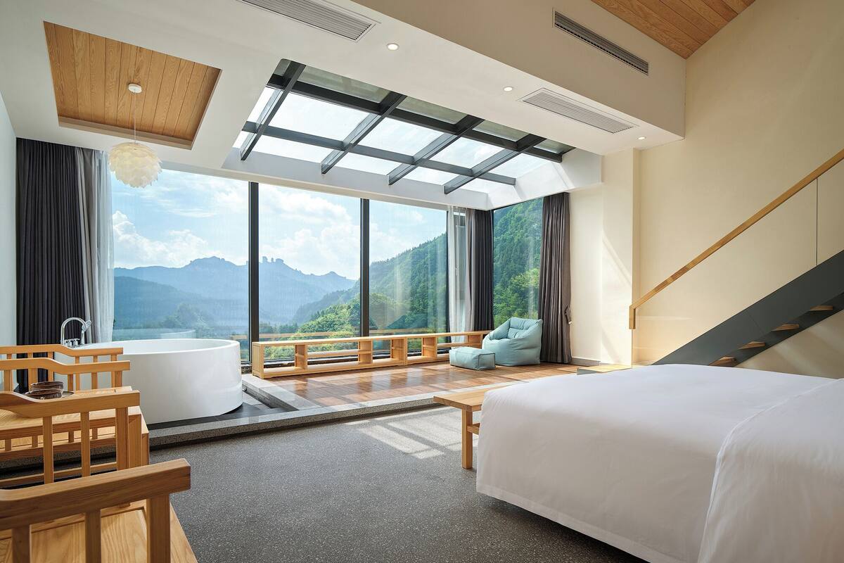 A modern bedroom with a large bed, a bathtub, and a view of mountains.