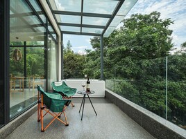 Ein moderner Balkon mit Glaswänden, einem Tisch, zwei Stühlen und einer Weinflasche.