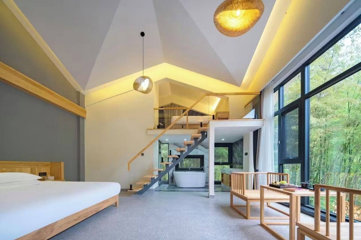 A modern bedroom with a large bed, a staircase leading to a loft, and a view of the outdoors.