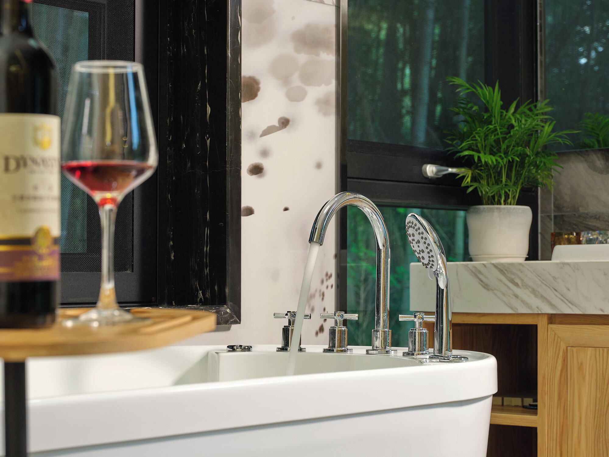 A modern bathroom with a large white bathtub, a glass wine glass, and a bottle of wine on the counter.