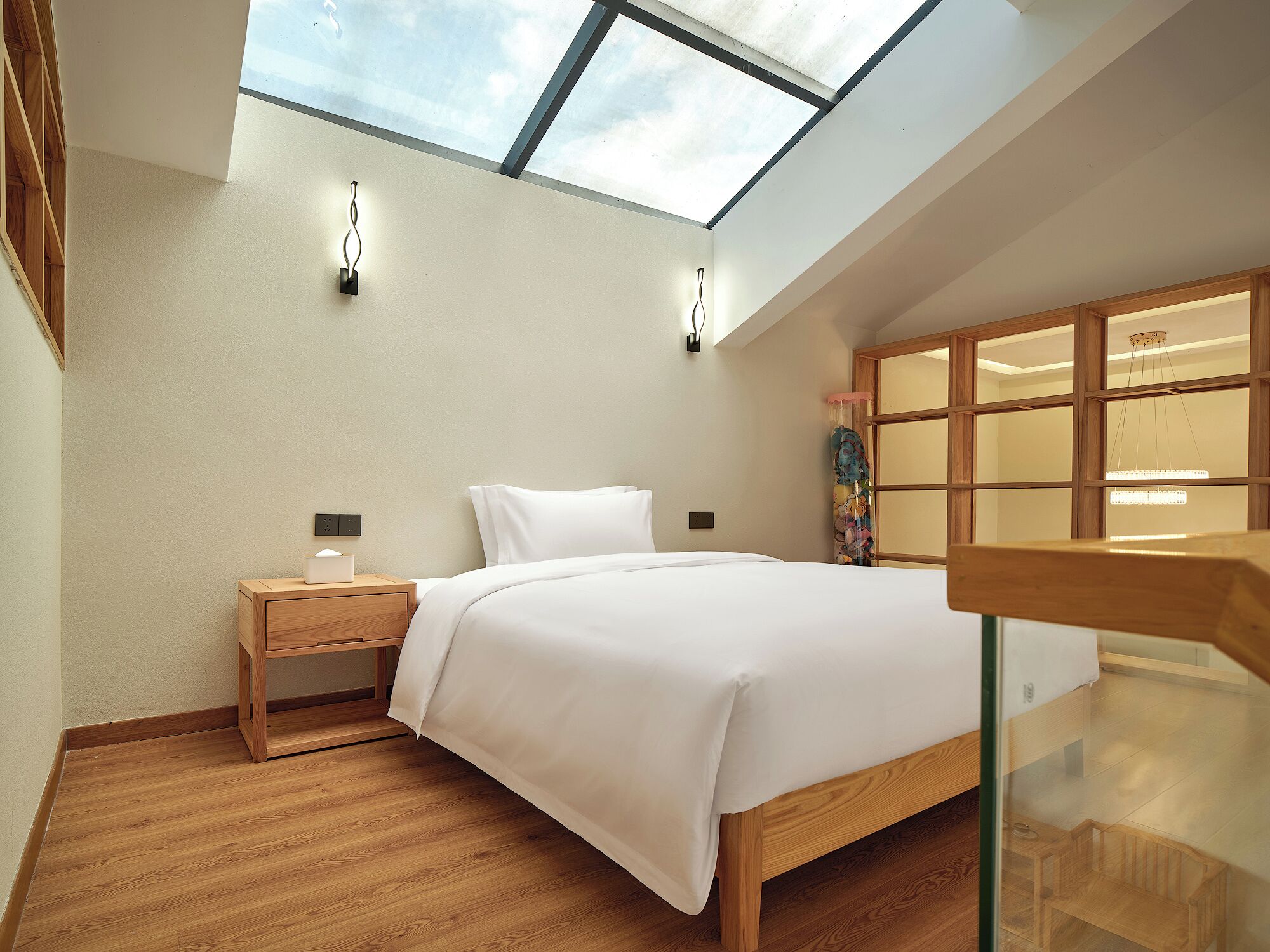 A bedroom with a skylight, wooden flooring, a bed with white bedding, a nightstand, and a wooden wardrobe.