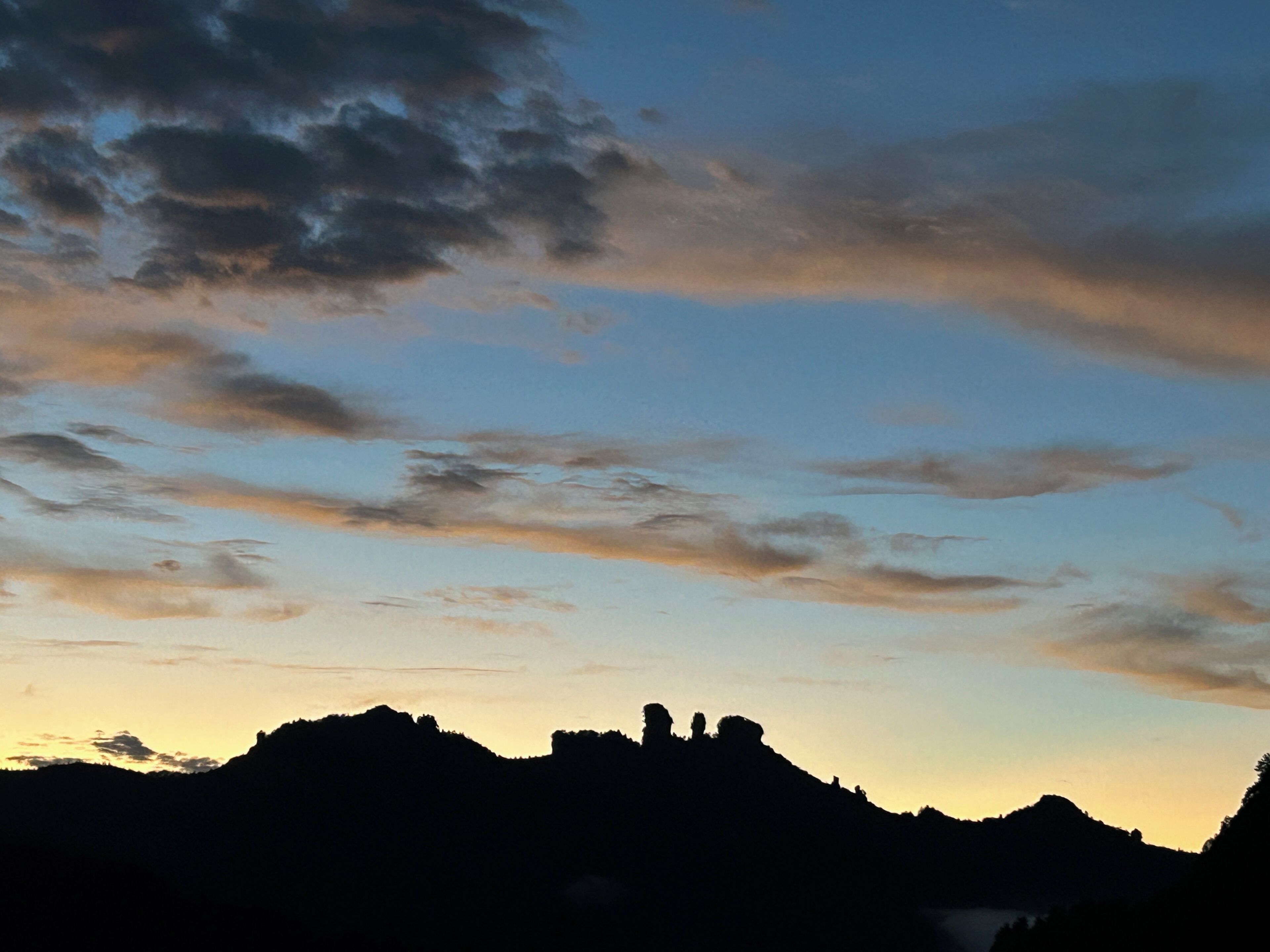 A silhouette of a mountain range against a sky with clouds.