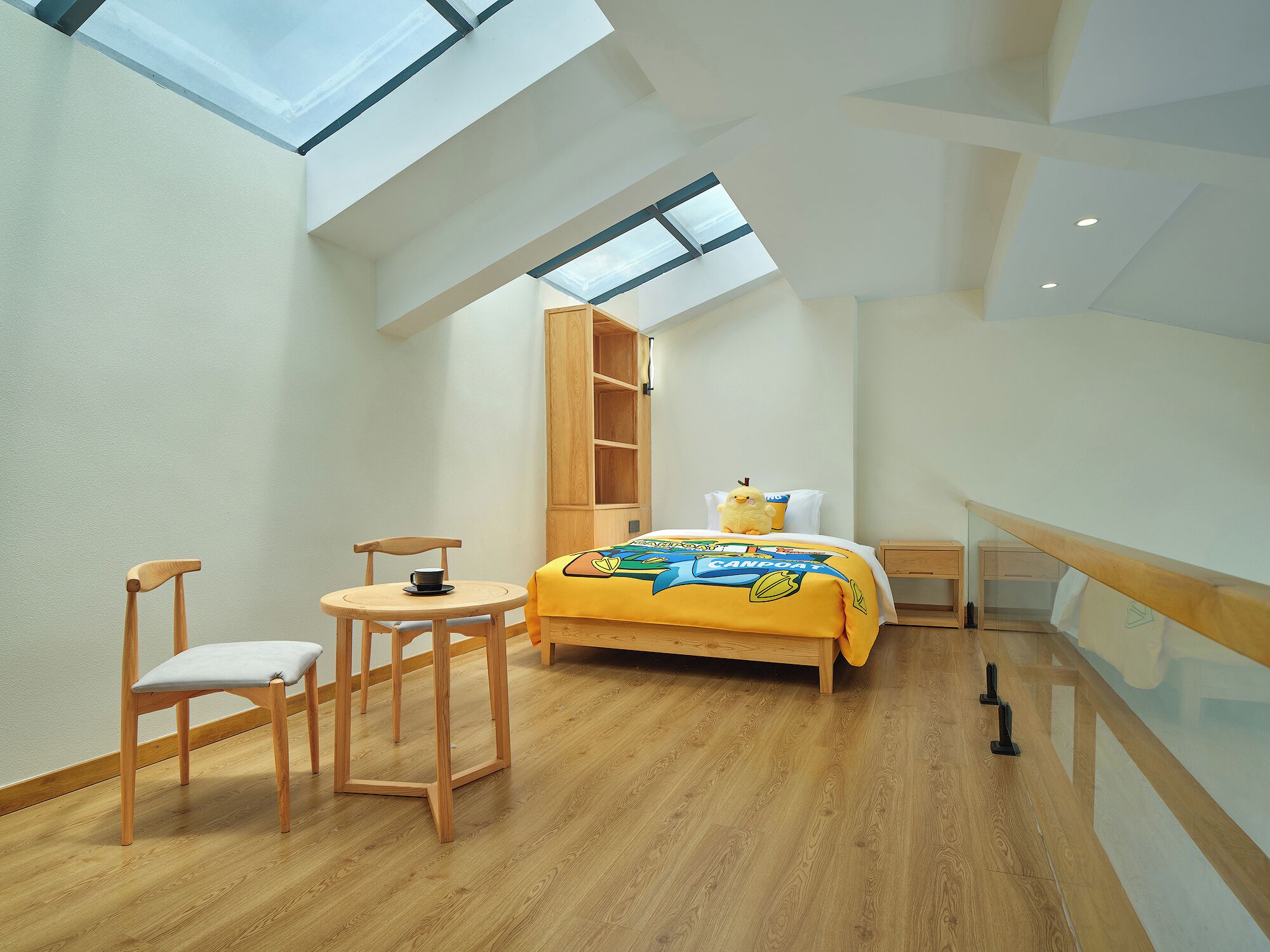 A room with a skylight, a bed with a yellow blanket, a wooden chair, and a small table.
