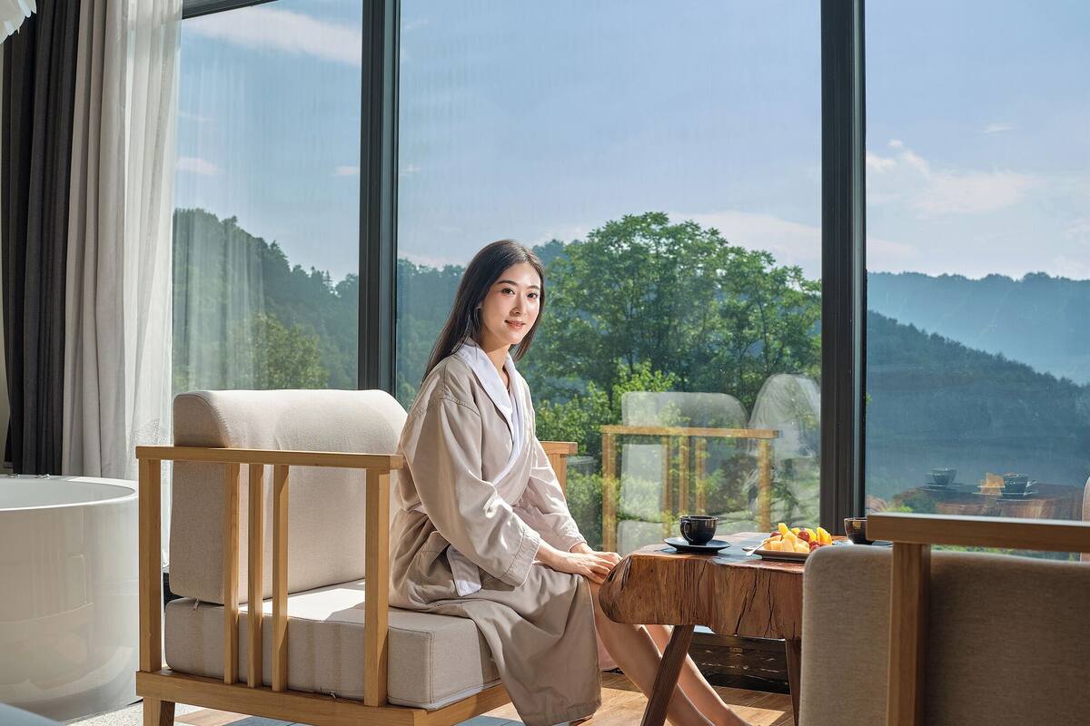 A person seated on a sofa with a view of a mountainous landscape through large windows.