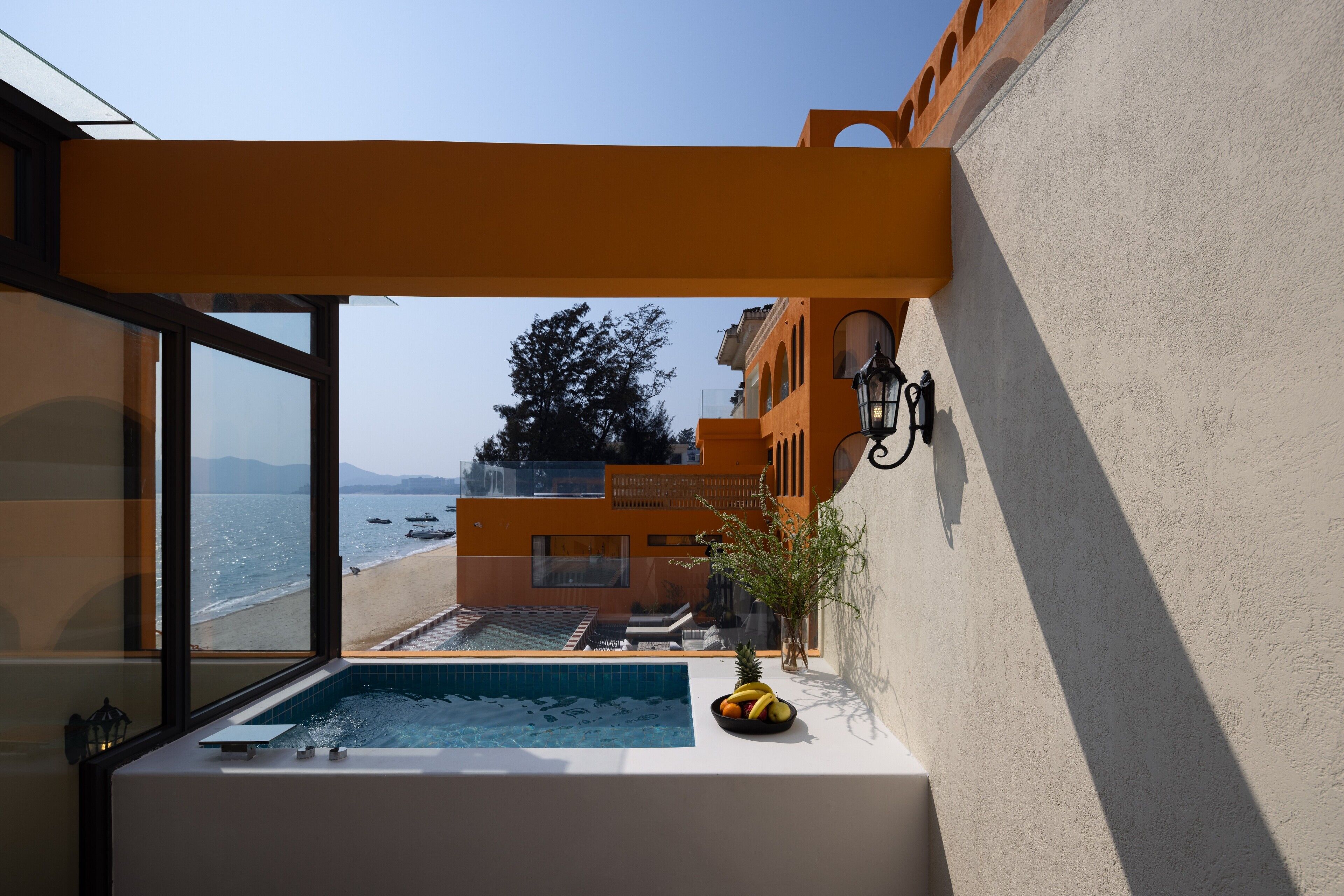 A balcony with a view of the beach and ocean, a small pool, and a potted plant.