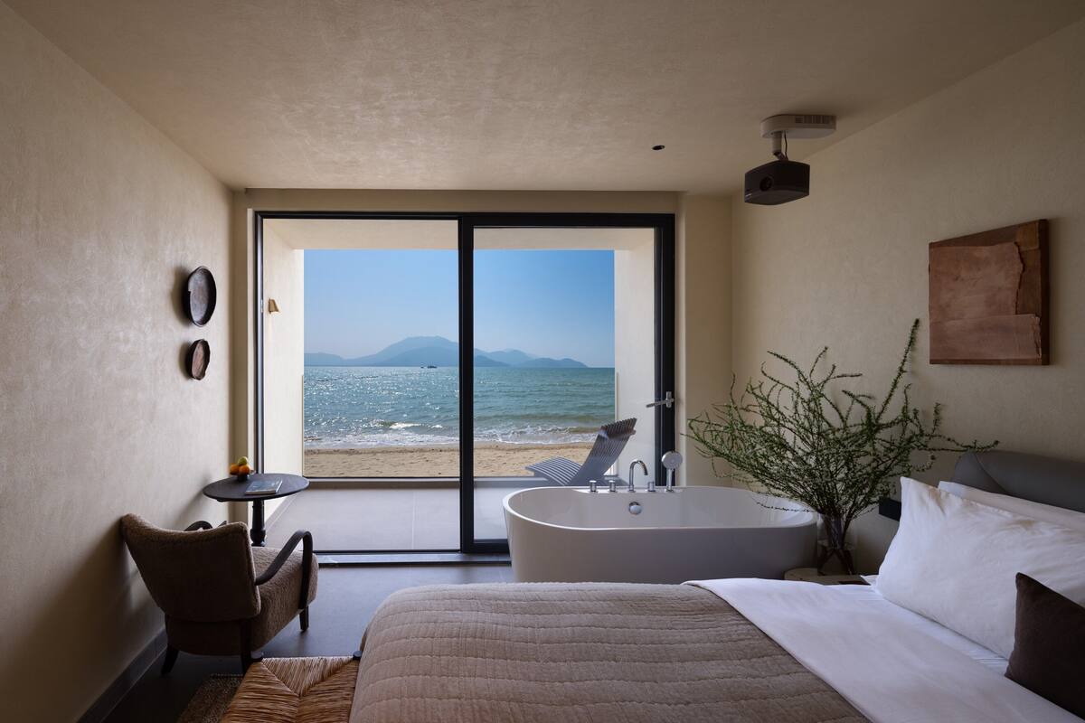 A bedroom with a large bed, a bathtub, and a view of the beach.