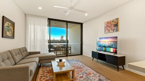 A modern living room with a sofa, coffee table, flat-screen TV, and a balcony with a view.