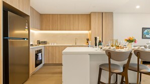 A modern kitchen with a central island, wooden cabinets, and a stainless steel refrigerator.