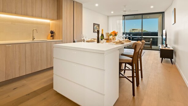 A modern kitchen with a central island, wooden cabinetry, and a dining area with a view.